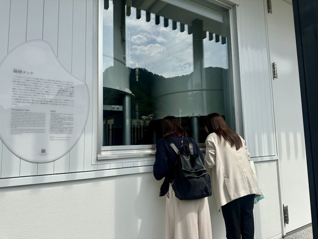吉峯蔵の解説パネルと、外から設備を覗く酒小町メンバー